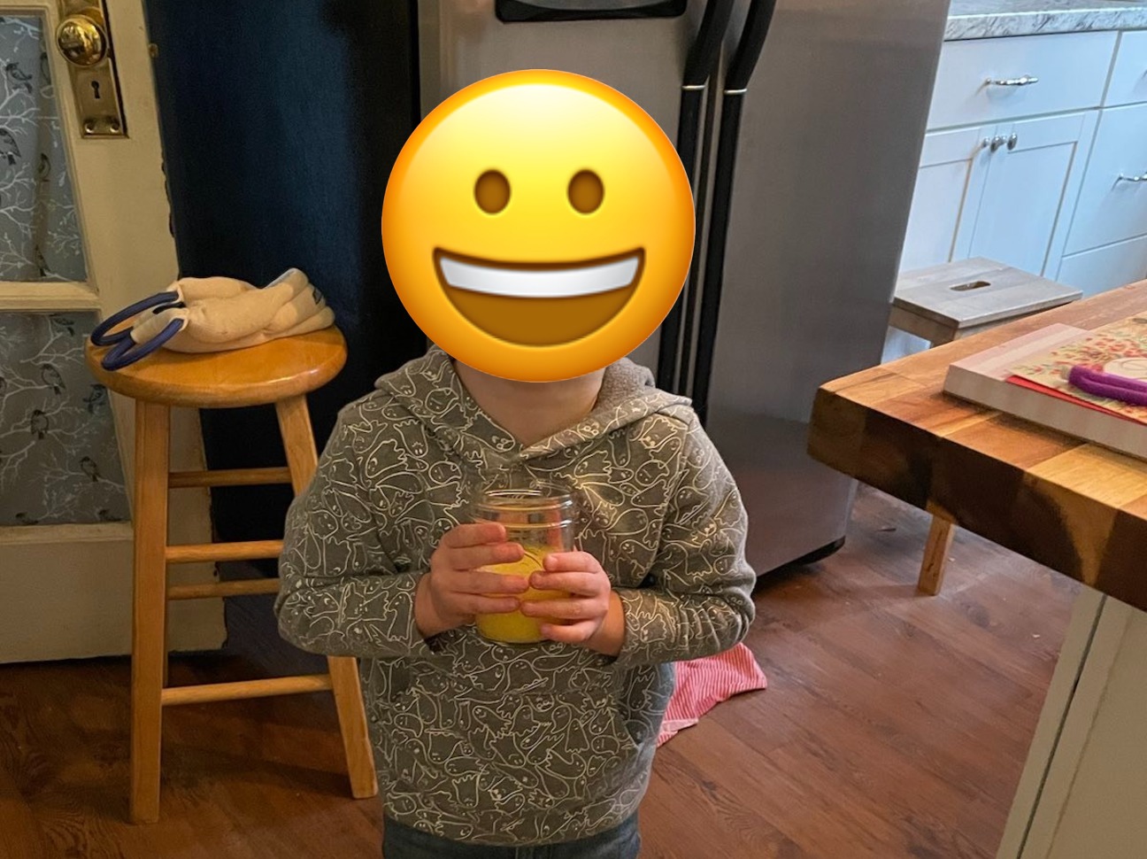 A child cheeses for the camera while holding a glass of orange juice.